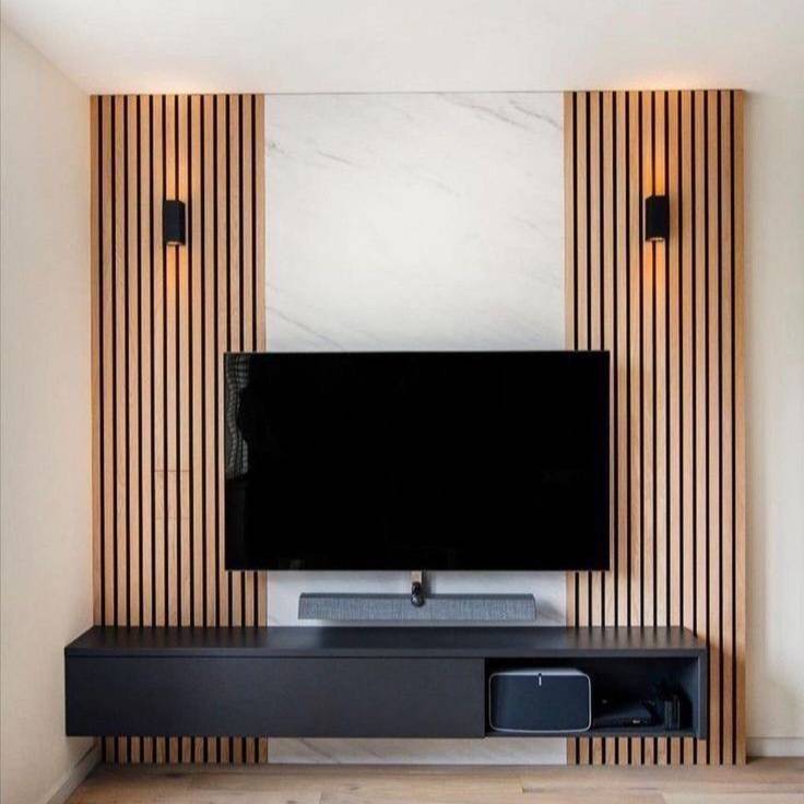 A modern wall-mounted TV stand setup with a black floating media console, a black flat-screen TV, and a soundbar, set against a decorative wall featuring vertical wood slats, a white marble panel, and warm sconces.